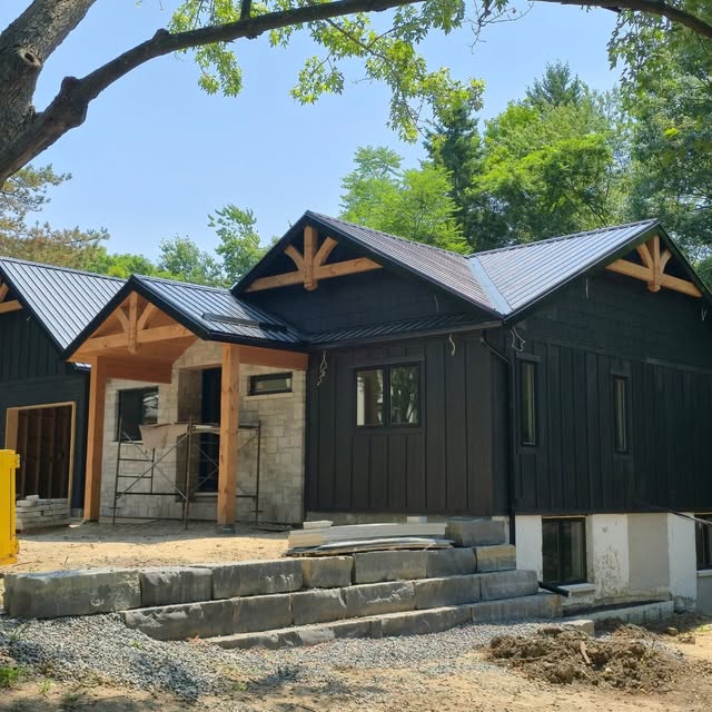 Custom home with black board-and-batten siding, standing-seam metal roof, timber gable trusses and a stone entry, with limestone slab steps