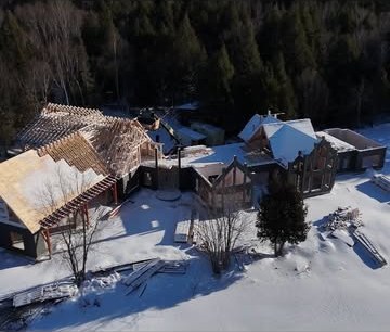 Aerial winter view of a new roof structure being framed and sheathed beside a large existing stone house