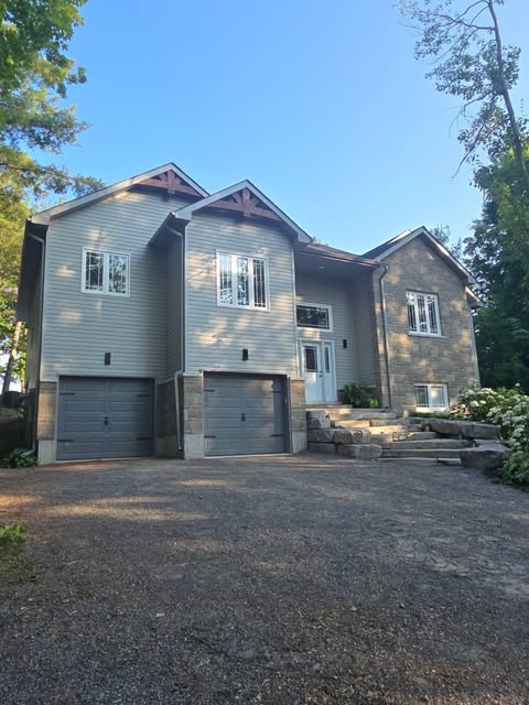Finished two-storey home with stone and horizontal siding, timber gable brackets, and two garage doors