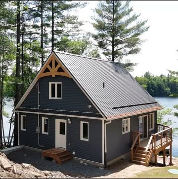 Completed navy-sided lakeside home with a grey metal roof and a timber truss in the gable
