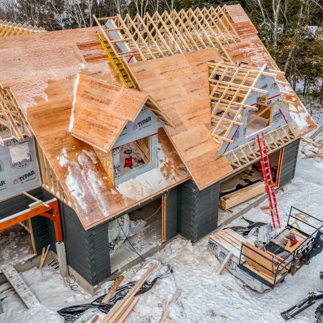 Aerial view of roof framing and sheathing going on over a house in winter