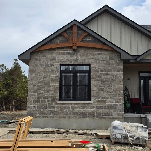 Stone gable end with an arched timber truss accent set into the gable above a black-framed window